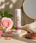 Rose tint balm by Whole Rituals on a wooden tray with flowers and a mirror in the background