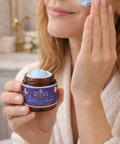 Woman applying a blue cream to her face with a jar of the same cream in her hand.