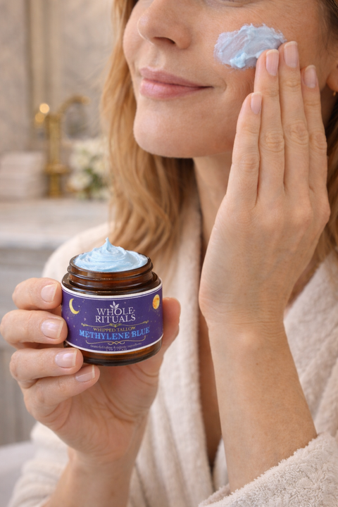 Woman applying a blue cream to her face with a jar of the same cream in her hand.