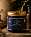 Jar of 'Whole Rituals' Methylene Blue on a wooden surface with plants in the background