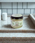 Jar of tallow balm on a bathroom counter with tiled wall in the background